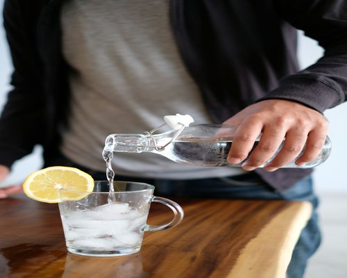 A person pouring water into a glass near a fresh homemade meal